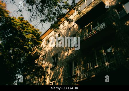 On a summer day, the warm and cozy light of the sun shines through the leaves of the trees and illuminates the apartment building. Stock Photo