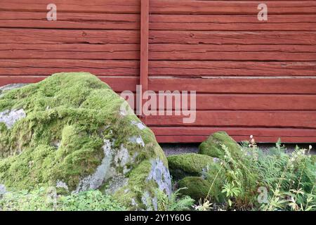 Moss-covered stones by a red wood barn wall in southern Finland, August 2024 Stock Photo