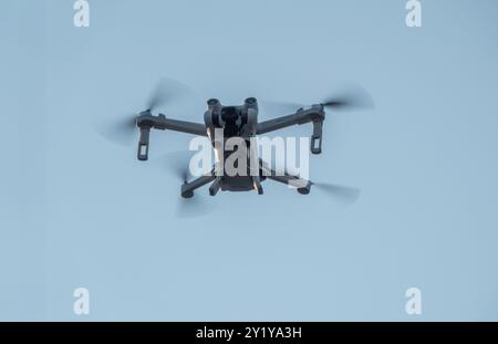 Drone with 4 spinning propellers in the flight seen from below. Blue sky background. Copenhagen, Denmark - September 6, 2024. Stock Photo