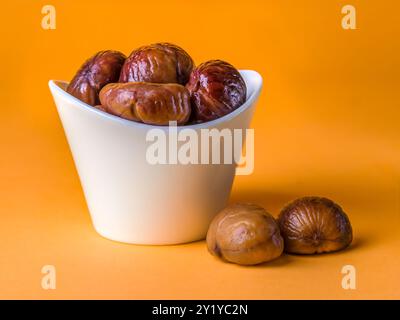 Bunch of Spanish chestnuts in white ceramic bowl on orange background Stock Photo