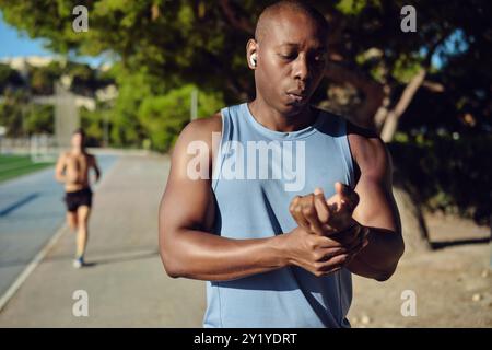 Serious jogger man standing outdoors and checking his heart rate or pulse with fingers, monitoring his health metrics, after workout. Health, sports c Stock Photo
