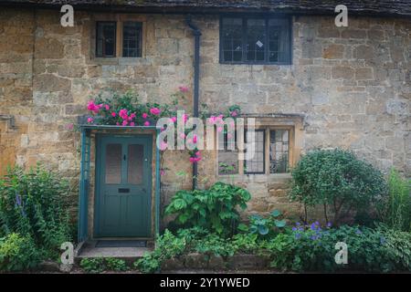 A picturesque view of a traditional stone cottage with a green door and windows, surrounded by blooming flowers and lush greenery, evoking a serene an Stock Photo