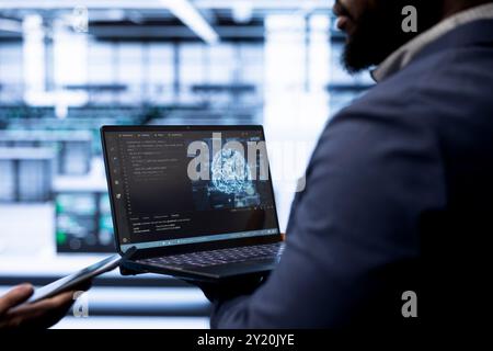 Engineer using AI software on laptop, programming in data center, updating neural networks. Close up shot of IT professional in modern server hub startup upgrading artificial intelligence systems Stock Photo