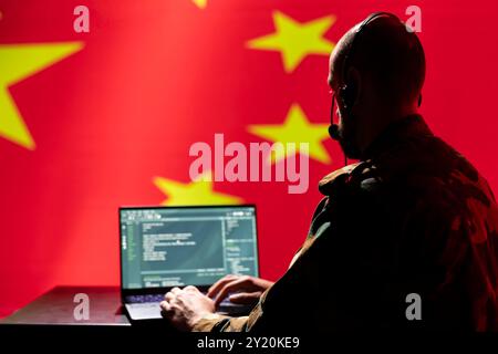 Chinese army telecommunication systems operator using radio and satellite tech, talking in headphones mic. China military dispatcher managing communications networks, typing on device Stock Photo