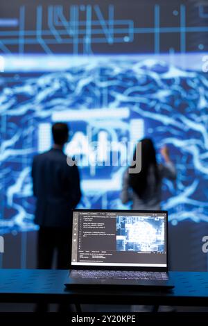 Focus on complex AI brain models being analyzed on laptop by developers in blurry background. Close up of machine learning on notebook used by teamworking IT staff members to develop AI Stock Photo