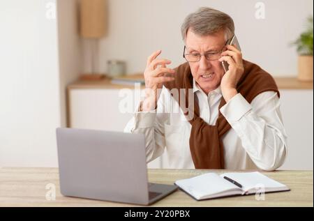 Discontented Senior Man Talking On Phone Sitting In Modern Office Stock Photo