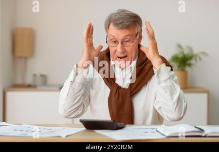 Shocked Senior Businessman Looking At Calculator Sitting In Office Stock Photo