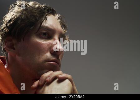 Portrait of young Caucasian man resting his chin on clasped hands while looking away, appearing thoughtful and introspective with slightly disheveled hair Stock Photo