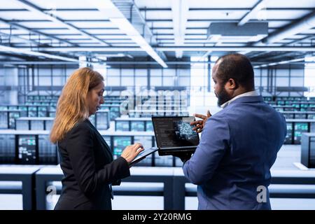 Teamworking colleagues using AI software on laptop, programming in AI data center. IT staff members in high tech server hub facility upgrading artificial intelligence systems Stock Photo
