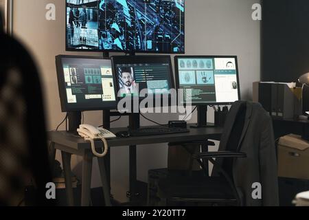Office space having multiple computer monitors displaying security footage and detailed information. Room filled with equipment and work essentials indicating active surveillance Stock Photo