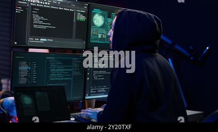 Hacker arriving in hidden underground shelter with laptop, prepared to launch malware attack on websites. Scammer in apartment starting work on dangerous script that can breach security, camera B Stock Photo