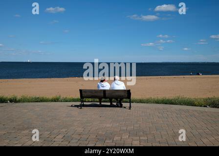 Older couple sitting on a bench overlooking Raritan Bay in South Amboy, New Jersey Stock Photo