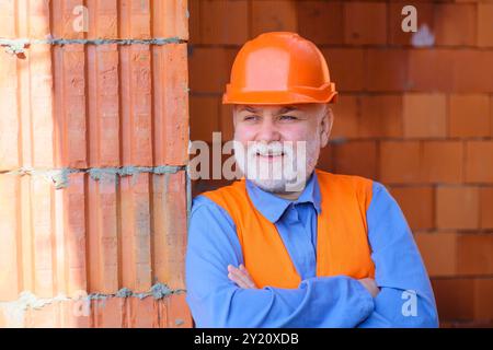 Smiling construction worker in safety vest and helmet. Bearded architect, engineer or builder in protective hard hat with crossed arms. Foreman or cra Stock Photo