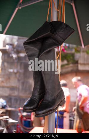 Black leather boots hanging at outdoor flea market, displayed boots, old town background concept Stock Photo