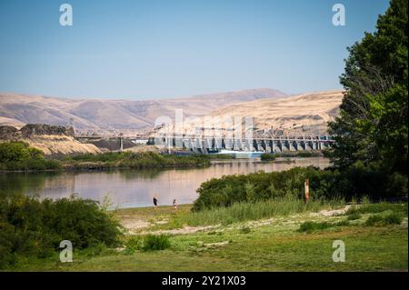 A family walks by with the Dalles Dam in the background.  The Dalles Dam on the Columbia River is one of the largest hydro electric dams in the USA. Stock Photo