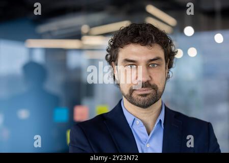 Businessman with serious expression standing in modern office setting, showcasing confidence and professionalism. Portrait reflects thoughtful attitude, suitable for corporate environments Stock Photo