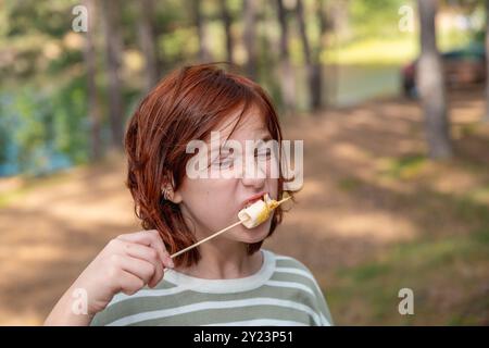 Cute girl eats marshmallows roasted over a campfire on a camping trip Stock Photo
