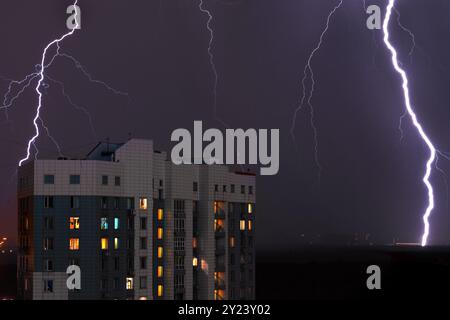 Thunderstorm with lightning bolt strikes and storm over city in purple light at night building with in the windows closeup Stock Photo