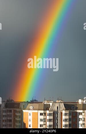 Bright colorful rainbow over city buildings in rainy day dark blue sky overcast weather background Stock Photo