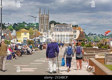 Teignmouth seaside resort wide promenade long row of popular seats back view adults walking & dog walk on lead in chilly June day out Devon England UK Stock Photo