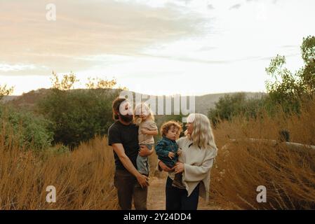 Family of four walks down nature trail at sunset Stock Photo