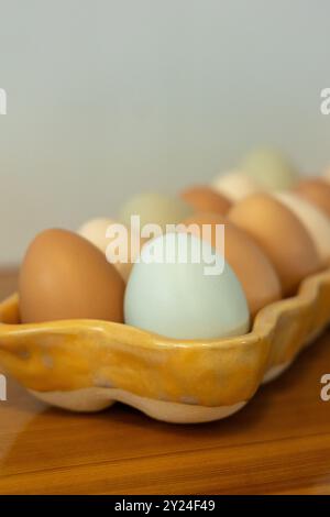 Close-up of multicolored eggs in a ceramic tray on a wooden table Stock Photo