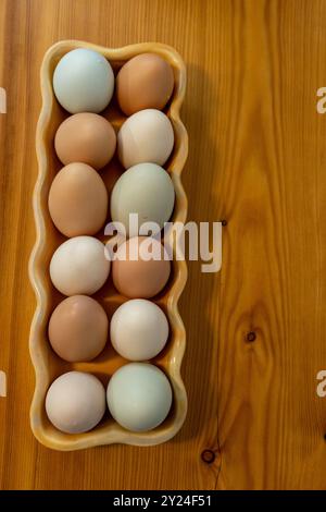 Top view of multicolored eggs in a ceramic tray on a wooden surface Stock Photo