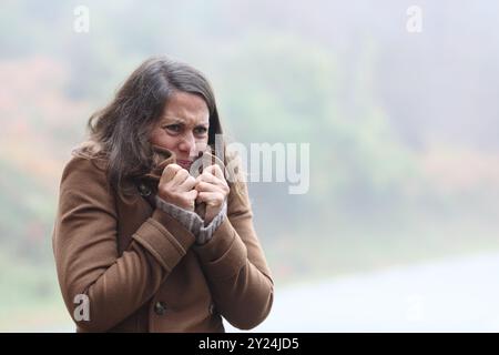 Middle aged woman getting cold grabbing jacket alone in winter Stock Photo