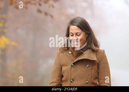 Happy middle aged woman walking and smiling in a park in winter Stock Photo