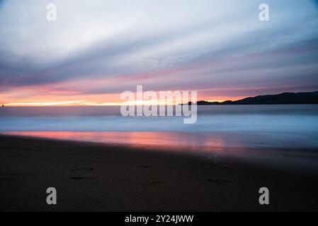 Ocean sunset with vibrant colors reflecting on water and sandy beach. Stock Photo