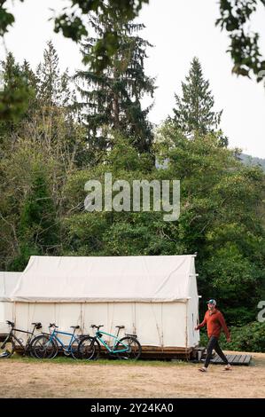 Man Walking Past Bicycles Near White Canvas Tent at Campground Stock Photo