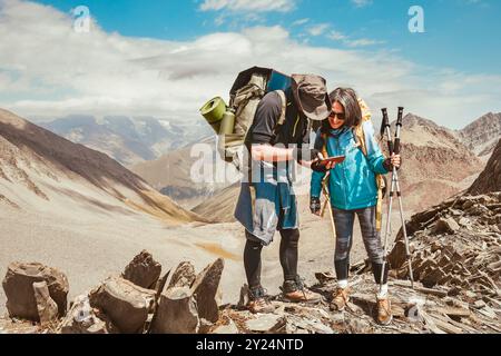 Attractive young Couple of hikers using a smartphone for orientation while out in mountains nature and wearing backpacks with camping gear. Trails tre Stock Photo