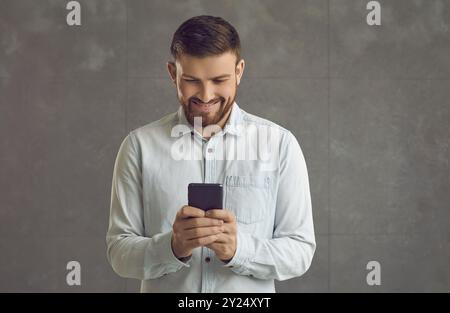 Satisfied phone user looking at smartphone screen standing isolated on grey background Stock Photo