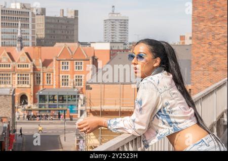 Indian woman in stylish denim outfit poses in an urban, architectural setting with geometric lines and cityscape views, blending fashion and life Stock Photo