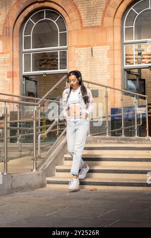 Indian woman in stylish denim outfit poses in an urban, architectural setting with geometric lines and cityscape views Stock Photo