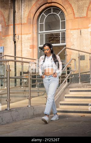 Indian woman in stylish denim outfit poses in an urban, architectural setting with geometric lines and cityscape views Stock Photo