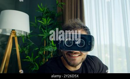 A funny man smiles while using a VR headset in a modern living room Stock Photo