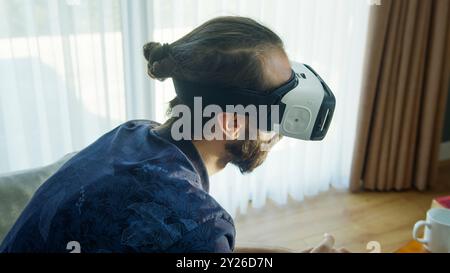 Bearded man wearing a VR headset explores virtual reality experience. Interacting with the virtual environment, the advanced technology's engagement. Stock Photo