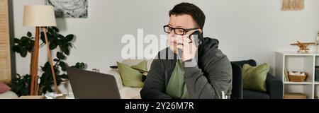 A young man with Down syndrome speaks on the phone while sitting at his desk. Stock Photo