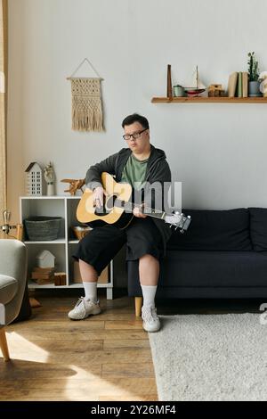 A young man with Down syndrome enjoys playing guitar in his cozy home. Stock Photo