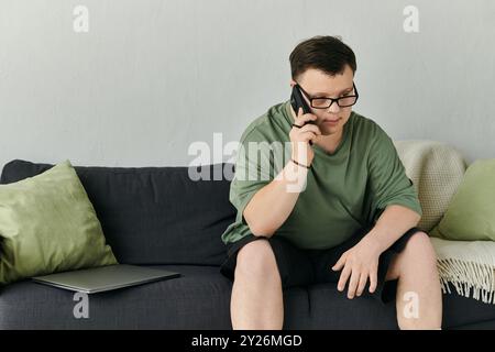 A thoughtful young man with Down syndrome speaks on the phone while sitting comfortably at home. Stock Photo