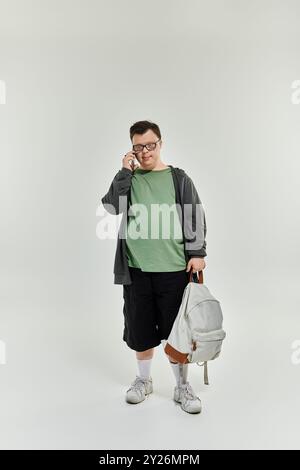 A young man with Down syndrome at home speaks on the phone with a backpack in hand. Stock Photo