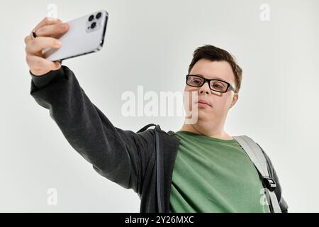 A young man with Down syndrome smiles confidently while capturing a selfie indoors. Stock Photo