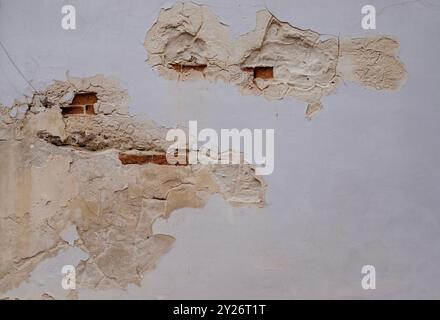 A close-up image of an aged wall showing areas where the paint has peeled away, revealing the underlying red brickwork. The rough, uneven textures of Stock Photo