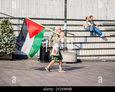 Stockholm, Sweden - September 7 2024: At Odenplan, a woman walks with a large Palestinian flag, its stick resting on her shoulder, during a public pro Stock Photo