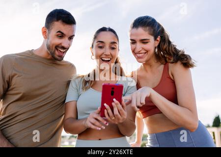 Three young sportive friends using mobile phone after workout routine outdoor Stock Photo