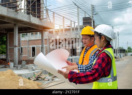 Team engineers holding blueprint project working outdoors building side with blueprints on a worksite, engineering and architecture concept, Engineers Stock Photo