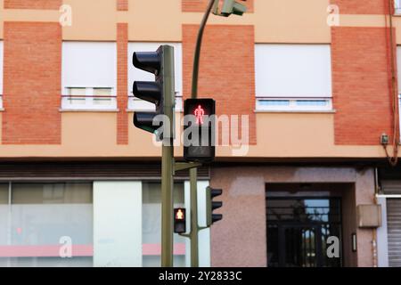 Red traffic light for pedestrian and green light for drivers on city street in front of building facade. Stop signal shows standing man figure on traffic light at pedestrian crosswalk. Regulations. Stock Photo