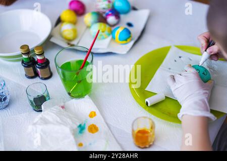 Close-up view of child drawing on Easter egg at table with supplies for decoration. Sweden. Stock Photo
