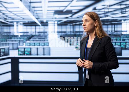 System administrator in data center workspace tracking network traffic and activity, looking at server rows. IT staff member performing database backups in high tech server room establishment Stock Photo